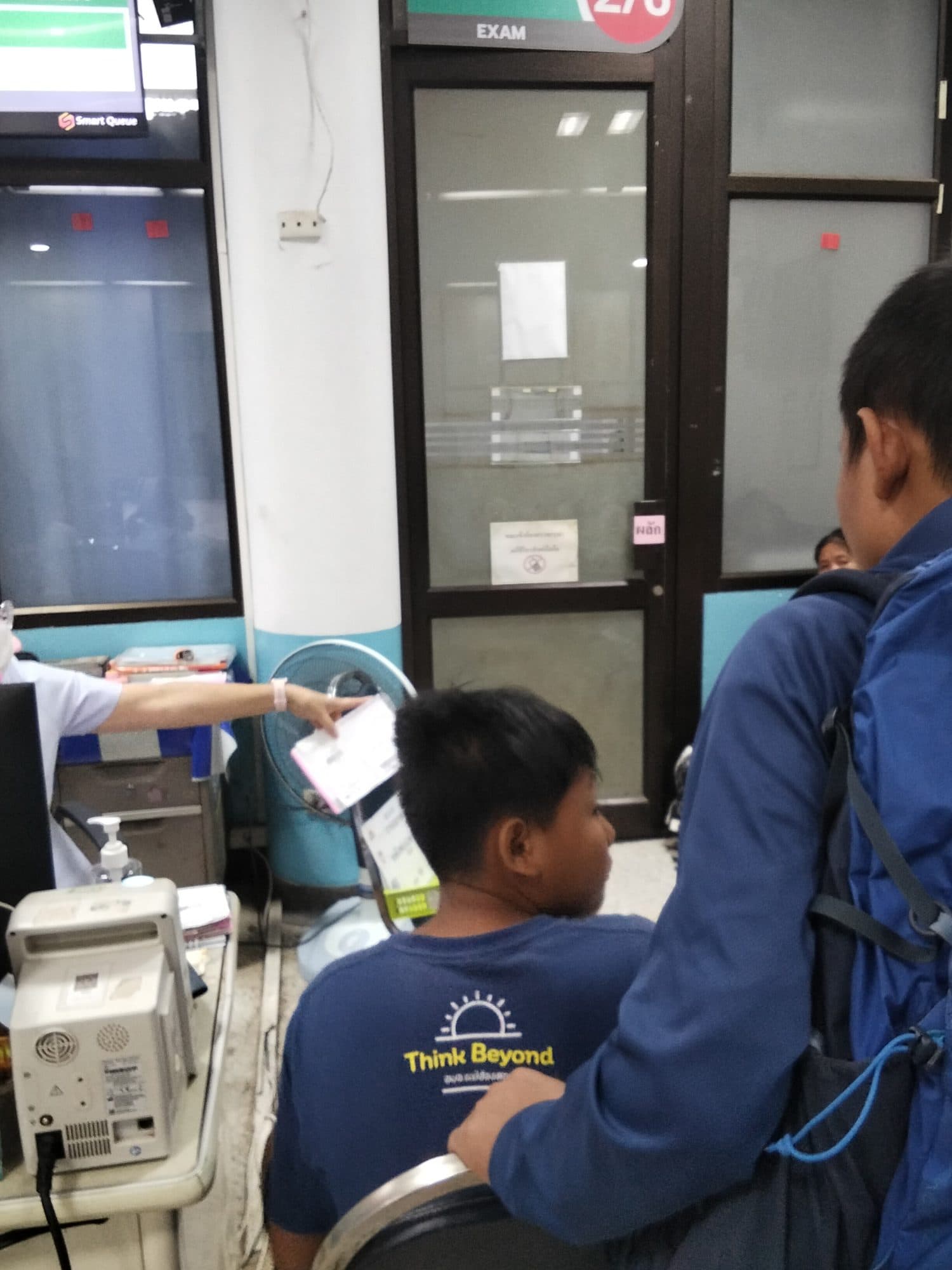 A young patient and companion at a hospital exam window, receiving medical paperwork.