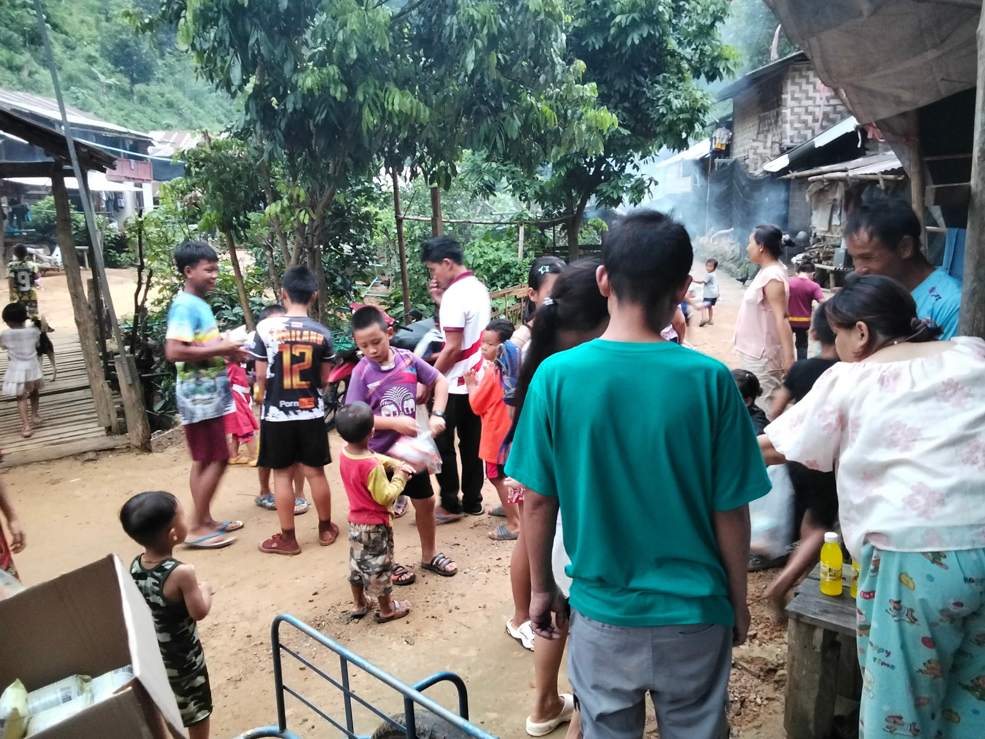 Neighbours and children gathered along the village lane in the evening as cooking smoke drifts between the homes.
